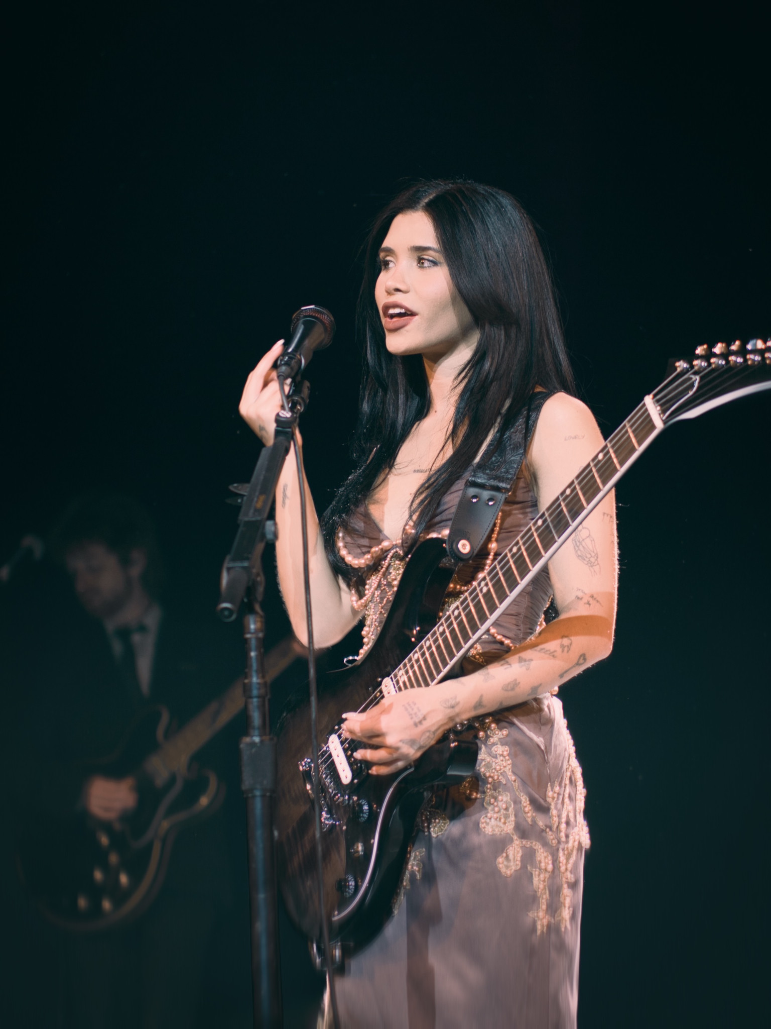 Nessa Barrett singing at a microphone with a guitar